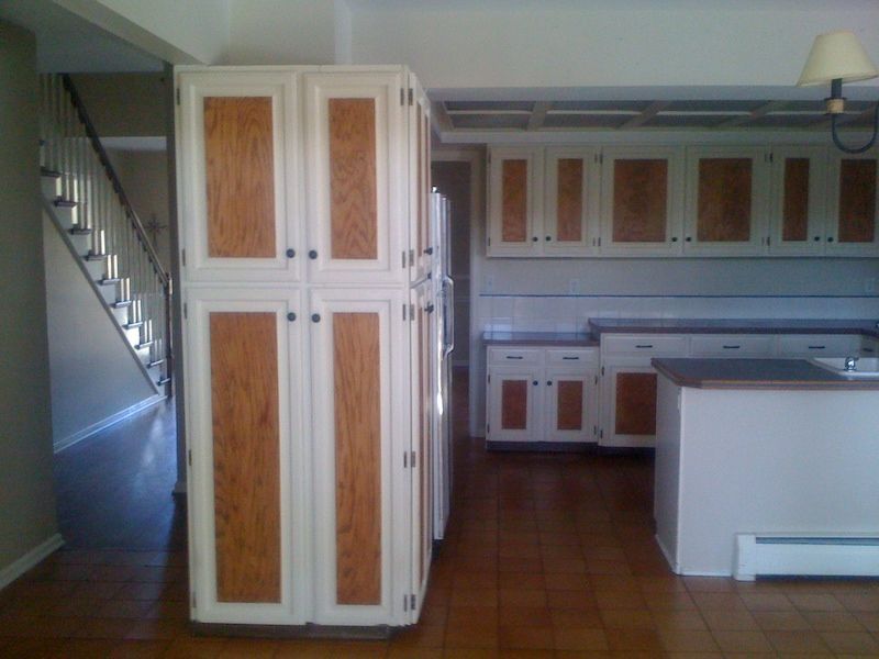 Kitchen with white cabinets and wood panel doors, brown tile floor, staircase in the background.