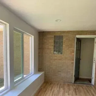 Sunroom interior with windows, brick wall, wood floor, and doorway.