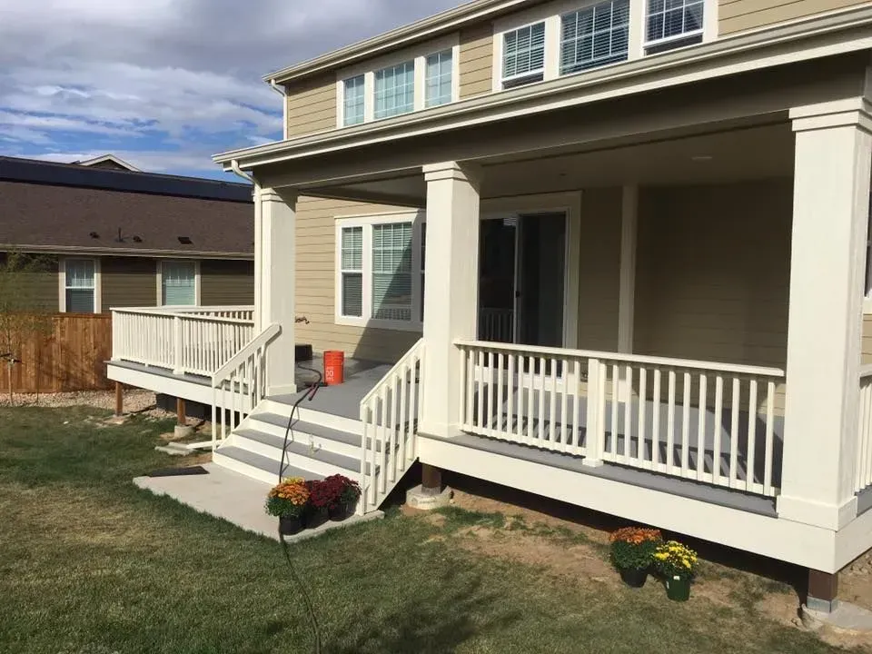 Backyard deck with stairs, railings, and covered porch. Beige siding, white trim, and colorful mums.