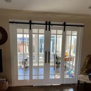 White French doors with black hardware, on a sliding track, leading to a sunlit room.