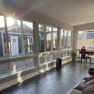 Sunroom interior with dark wood floor, rows of windows, and view of a yard.