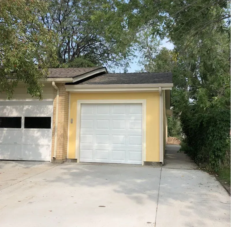 Yellow garage with white door and tan brick accent. Concrete driveway.