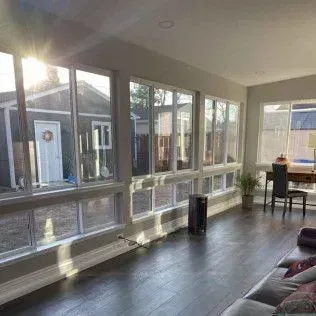 Sunlit room with large windows overlooking a backyard, dark wood floor, and a desk.