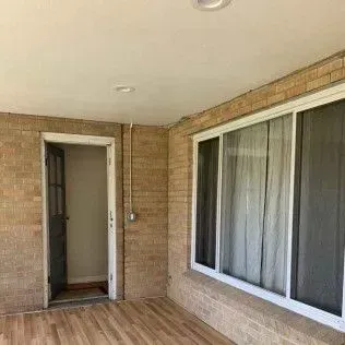 Sunroom interior with brick walls, sliding window with curtains, and an open doorway.