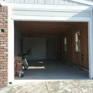 Open garage with exposed wooden interior, brick and white trim, concrete floor, light streaming in.