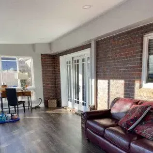 Interior of a room with brick wall, French doors, desk, and a burgundy sofa. Sunlit floor.