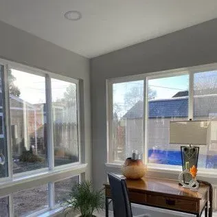 Sunroom with windows, desk, lamp, and potted plant. Bright sunlight illuminates the room.