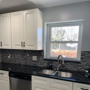 White kitchen cabinets with black countertops and gray backsplash next to a window over a sink.