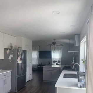 Kitchen interior with gray cabinets, stainless steel refrigerator, and white countertops.