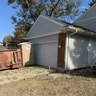 Exterior view of a garage with a dumpster and portable toilet.