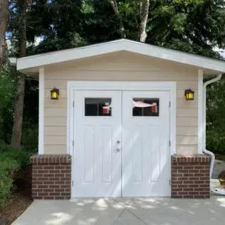 Tan garage with white double doors, brick accents, and outdoor lights.