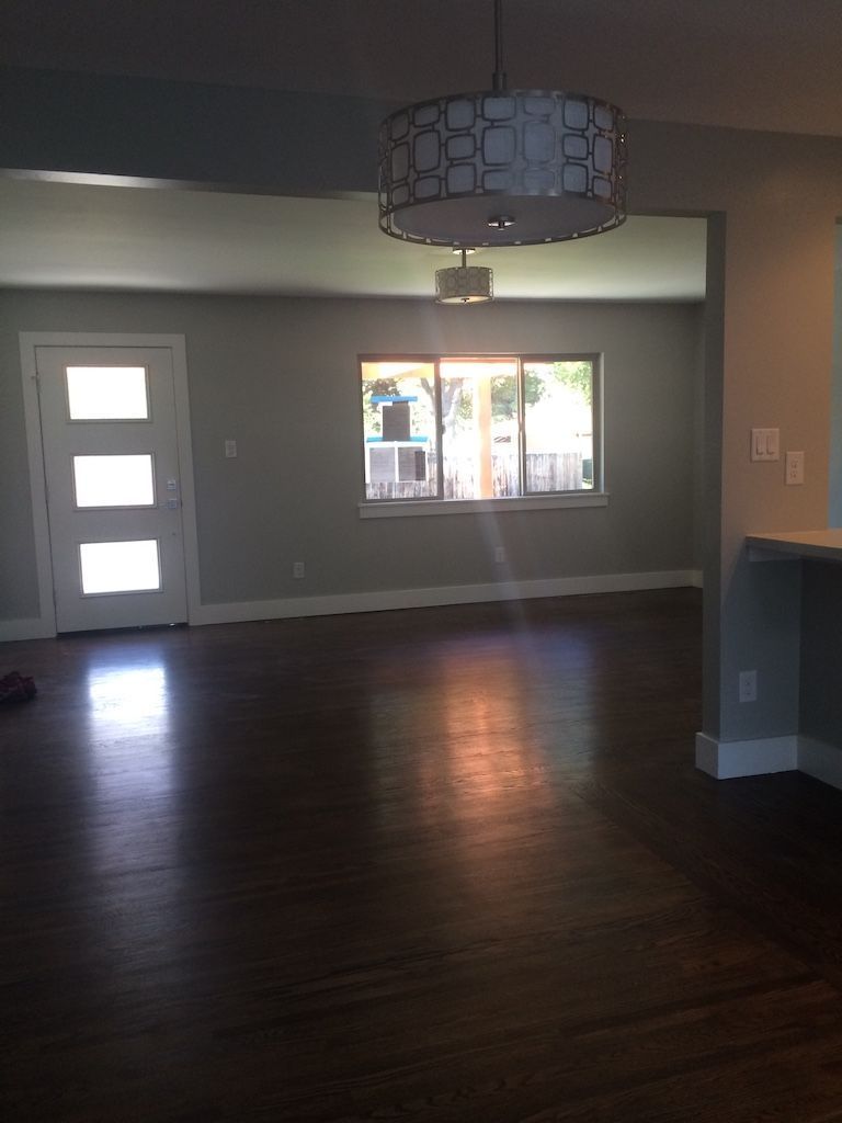 Interior view of a living space with dark wood floors, light gray walls, and a window letting in sunlight.