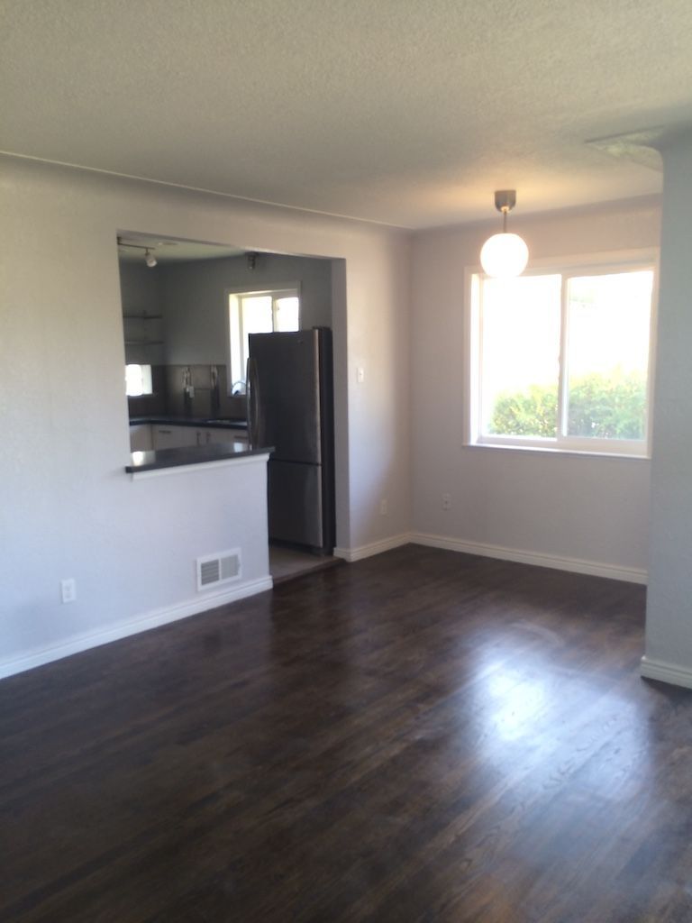 Dining room with dark wood floors, light gray walls, and a view into the kitchen.