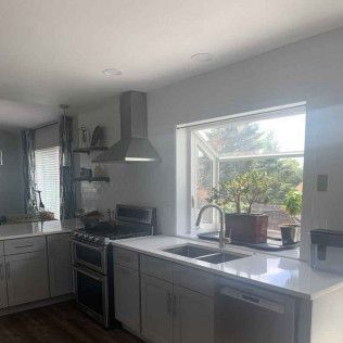 Modern kitchen with white cabinets, stainless steel range hood, and large window.