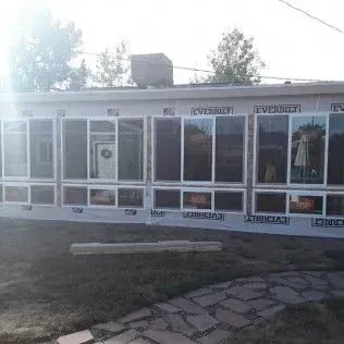 Sunroom addition to a house with large windows, covered in Tyvek, on a sunny day.