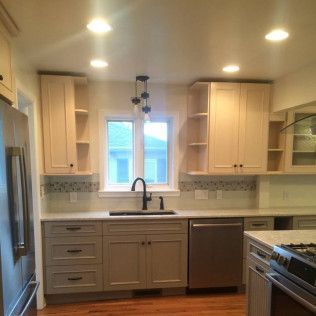 A newly remodeled kitchen with light wood cabinets, grey lowers, stainless steel appliances, and a window above the sink.