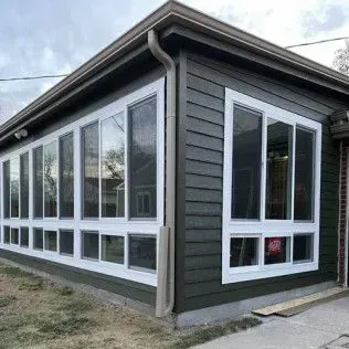 Corner of a building with multiple large, white-framed windows and green siding.