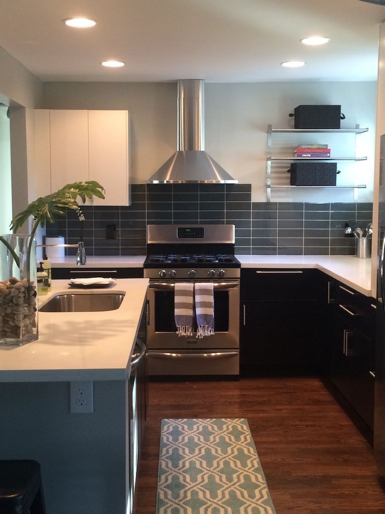 Modern kitchen with stainless steel appliances, dark cabinets, and a blue patterned rug.
