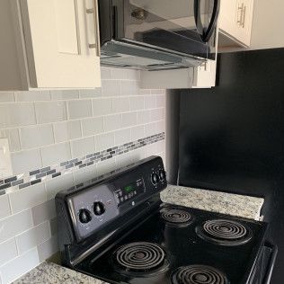 Kitchen with stove, microwave, cabinets, backsplash, and black refrigerator.