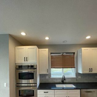 White kitchen cabinets with stainless steel appliances. Black countertops, white sink, and window with blinds.