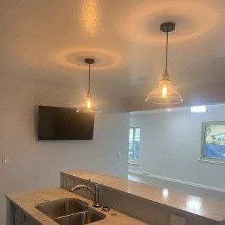 Kitchen with pendant lights above a countertop, sink, and mounted TV. Open to living space with painting.