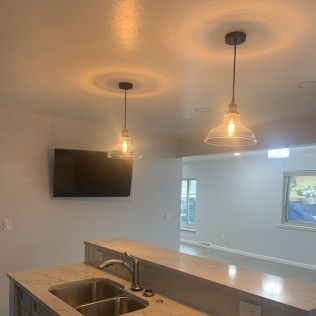 Two pendant lights above a kitchen island, with a TV on the wall. A sink is in the island.