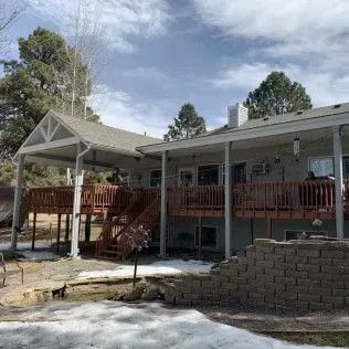 A house with a large deck and covered patio, surrounded by trees and snow on the ground.