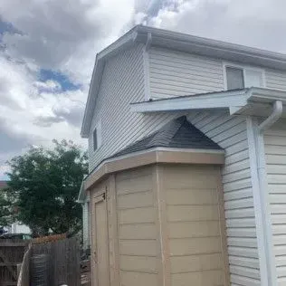 Beige two-story house with attached tan shed under a cloudy sky.