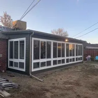 Sunroom addition to a brick house with many white framed windows, dark green trim, and a yard.