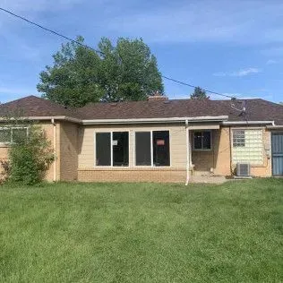 Back view of a beige brick house with a brown roof and a green lawn under a blue sky.