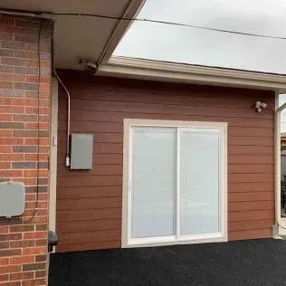 Brown siding and white sliding door on building, brick wall, electrical boxes.