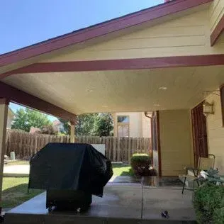 Covered patio with grill, looking out at a yard. The roof is tan and maroon.