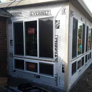 A building under construction with windows and Everbilt sheathing, attached to a brick wall.