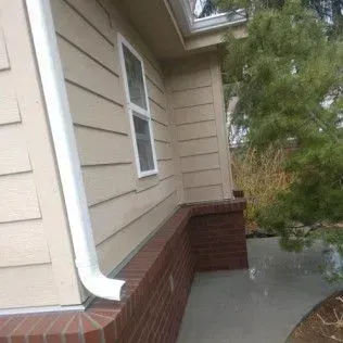 Exterior view of a beige house with white trim, brick foundation, and a white gutter.