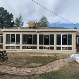 Exterior view of a home addition with large windows, tan siding, and a backyard with a stone path and grass.