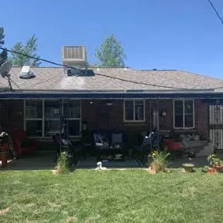 Backyard view of a brick house with a green lawn, patio furniture, and a dog lying down.