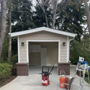 Tan garage with brick accents, open door, concrete driveway, tools and ladder visible.