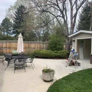 Patio with table, chairs, umbrella, shed, and greenery in backyard.