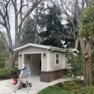 Beige garage with open door, brick base, window, and trees.