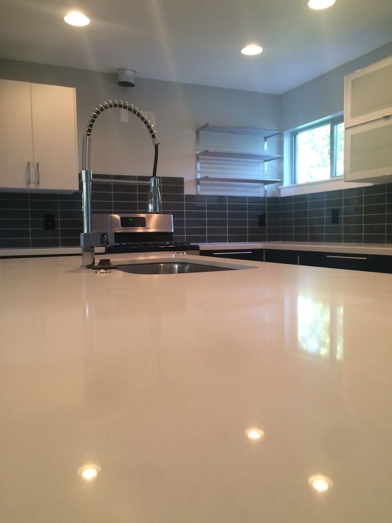 Kitchen with stainless steel faucet, white countertops, dark gray tiled backsplash, and white cabinets.