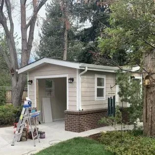 Tan detached garage with a brick base, open door, window, and exterior lights.