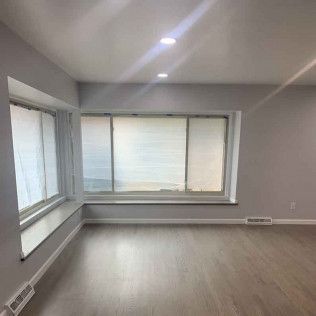 Empty room with large windows, light gray walls, and wood-look flooring.