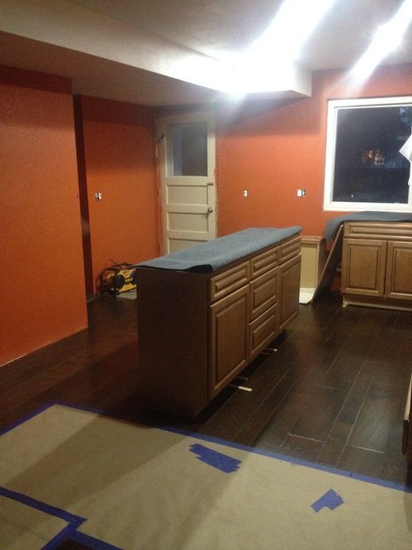Kitchen renovation in progress: Brown cabinets, orange walls, dark wood floor, covering on the floor.