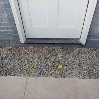 White door with a gravel bed at the base, bordered by a concrete walkway.