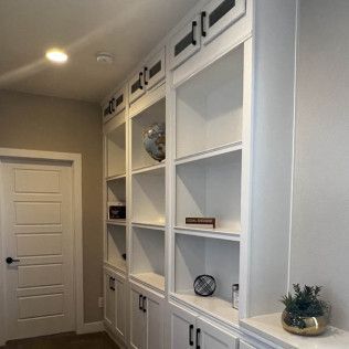 White built-in bookshelves with black hardware in a room. A closed door is on the left.