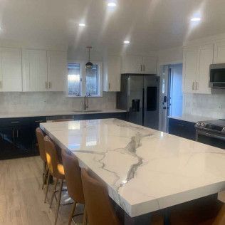 Modern kitchen with white and black cabinets, marble island with seating, and stainless steel appliances.