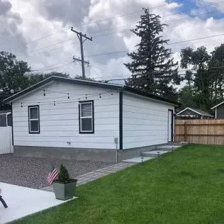 White building with black trim, windows, and door, next to a grassy lawn with a walkway.