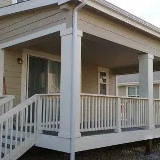 Beige house with white porch, columns, railings, and stairs.