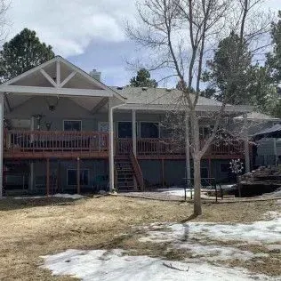 Back view of a house with a wooden deck and covered porch; some snow on the ground.