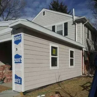 Side view of a house addition with tan siding and white trim; construction materials visible.